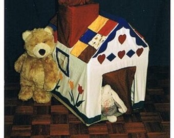 Könnte beinhalten: Ein weißes und rotes Spielhauszelt mit einem braunen Schornstein und einem herzförmigen Dach. Ein brauner Teddybär steht neben dem Zelt. Ein weißes Kaninchen befindet sich im Zelt.