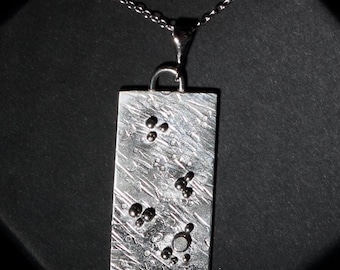 May include: A silver pendant necklace with a rectangular tag featuring a textured surface and small silver beads arranged in a pattern.