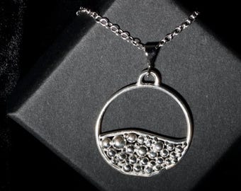 May include: A silver necklace with a round pendant featuring a textured design of small circles. The pendant is suspended from a silver chain.