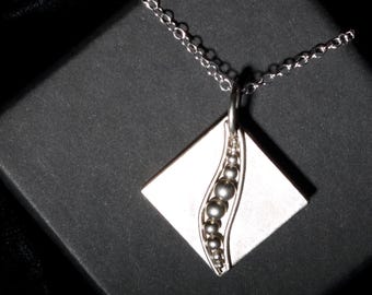 May include: A silver necklace with a square pendant featuring a curved line of silver beads. The pendant is on a silver chain.