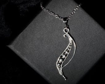 May include: A silver pendant necklace featuring a stylized leaf design with a series of small, round beads. The pendant hangs from a delicate chain. The necklace is displayed on a dark, textured surface, creating a contrast with the bright silver.