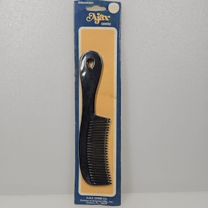 May include: A black Ajax comb on its original packaging. The comb has a handle with a hole and fine teeth. The packaging is blue and gold with the text "Unbreakable" and "Ajax combs".