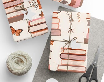 Pode incluir: Um conjunto de três papéis de embrulho com uma pilha de livros, borboletas e detalhes florais. Os papéis são brancos com detalhes marrons, laranja e rosa.