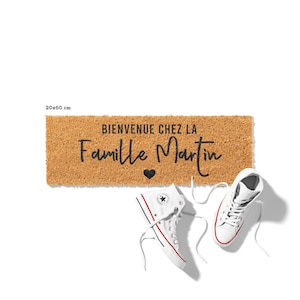 May include: A rectangular doormat, 20x60 cm, made of natural fibers, features the text "BIENVENUE CHEZ LA Famille Martin" in black script with a heart symbol. Two white high-top sneakers with red and black accents are placed near the mat.