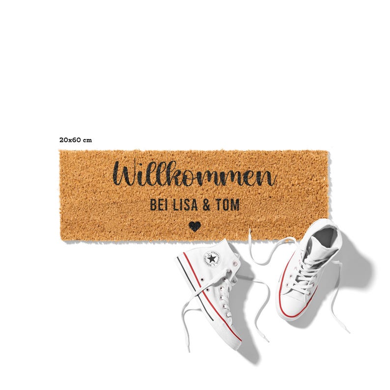 May include: A brown coir doormat with the text "Willkommen bei Lisa & Tom" and a small heart. The doormat is 20x60 cm.