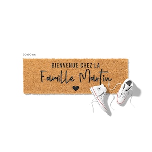 May include: A rectangular coir doormat, 30x90 cm, with the text "BIENVENUE CHEZ LA Famille Martin" in black script, a black heart, and a pair of white high-top sneakers with red and blue accents.