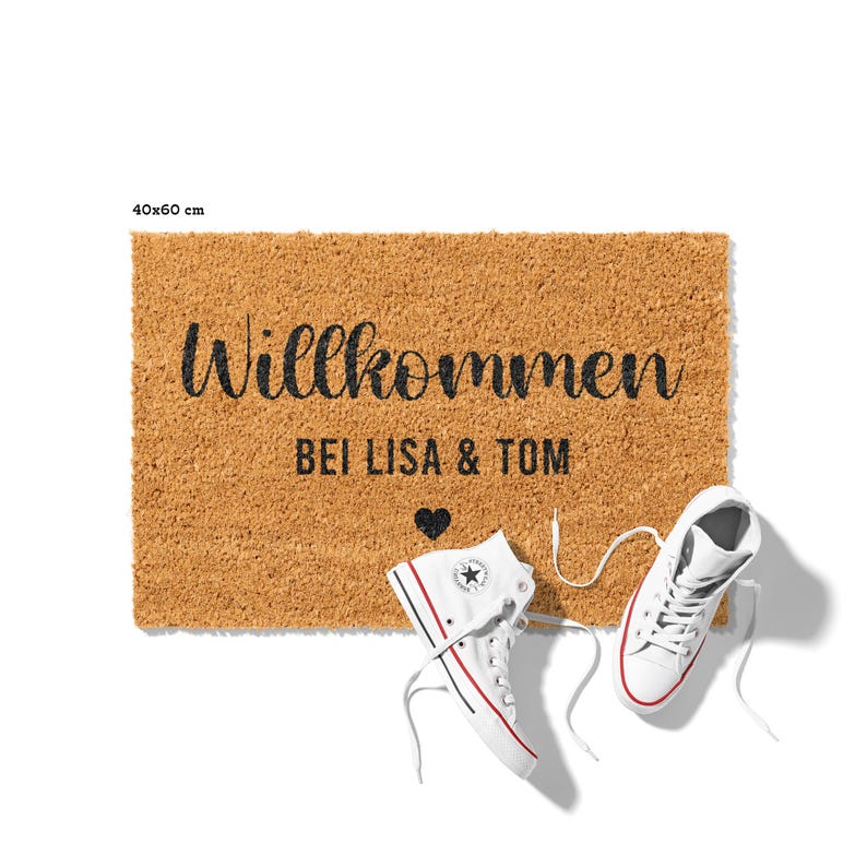May include: A brown coir doormat with the text "Willkommen bei Lisa & Tom" and a small heart. The doormat is 40x60 cm.
