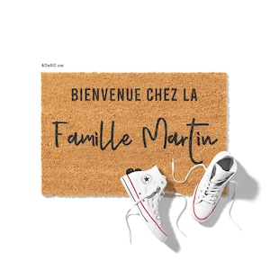May include: A rectangular doormat made of natural fibers, measuring 40x60 cm, with the text "BIENVENUE CHEZ LA Famille Martin" in black. Two white high-top sneakers with red and blue accents are placed near the mat.