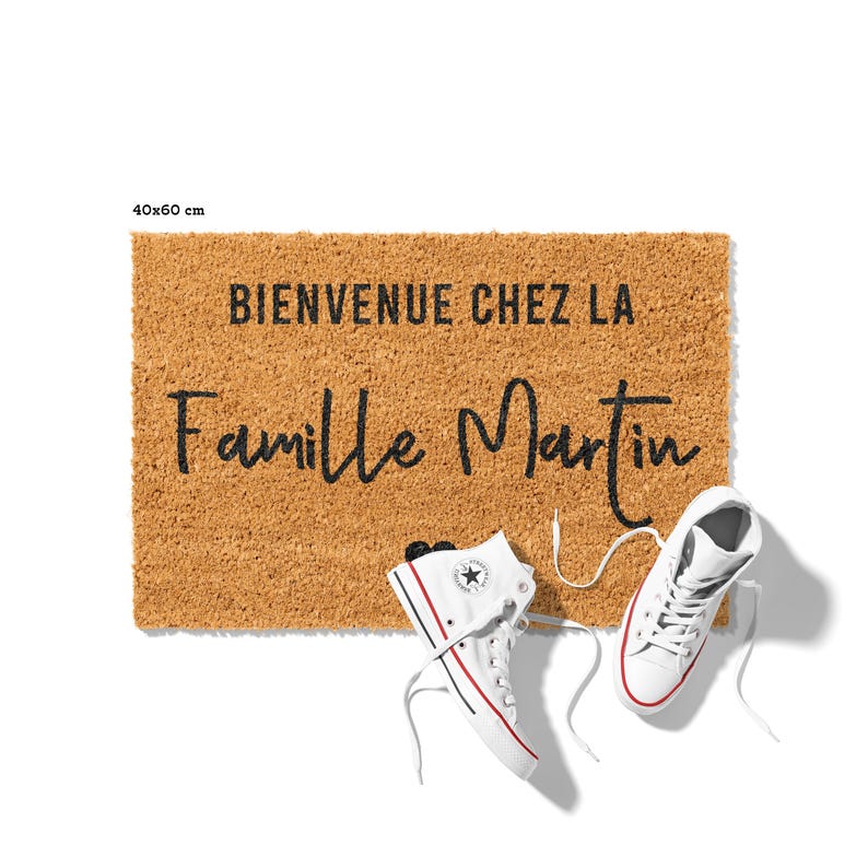 May include: A rectangular doormat made of natural fibers, measuring 40x60 cm, with the text "BIENVENUE CHEZ LA Famille Martin" in black. Two white high-top sneakers with red and blue accents are placed near the mat.