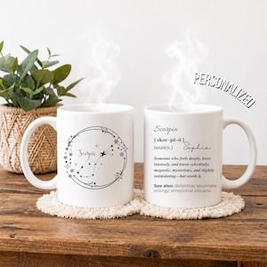 May include: Two white ceramic mugs featuring black text and graphics. One mug displays a Scorpio constellation within a circular floral wreath. The other mug shows a dictionary-style definition for Scorpio with the name Sophia and the text PERSONALIZED.