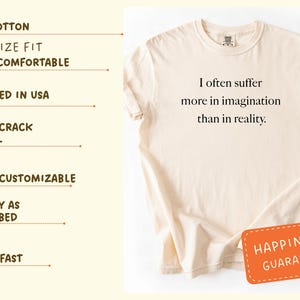 May include: Cream-colored t-shirt with the quote "I often suffer more in imagination than in reality." The shirt has an oversized fit and is made of 100% cotton. A small orange tag with the words "Happiness Guarantee" is attached.