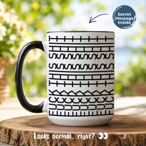 May include: A white ceramic mug with a black handle and interior, featuring a repeating black geometric pattern and the text "FUCK THIS SHIT" integrated into the design. A circular graphic in the top right corner states "Secret Message Inside".