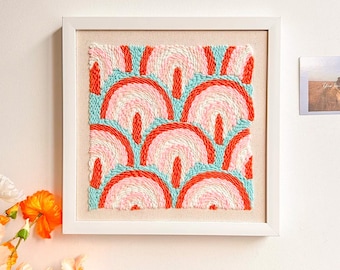 Puede incluir: Una pieza de arte de pared enmarcada con un diseño abstracto colorido. El diseño presenta un patrón repetitivo de arcos en tonos de rosa, naranja y azul.