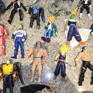May include: A collection of action figures, including a red and white Power Ranger, a race car driver, and various superhero and monster figures. The figures are made of plastic and have detailed designs, with a variety of colors and poses.