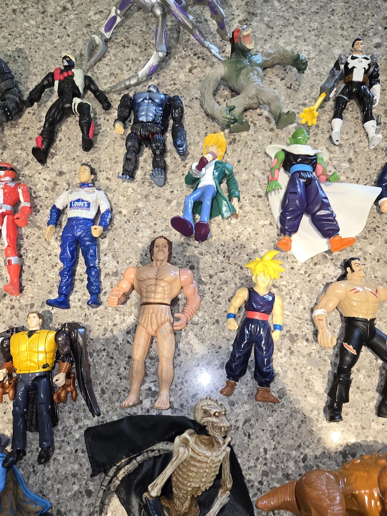 May include: A collection of action figures, including a red and white Power Ranger, a race car driver, and various superhero and monster figures. The figures are made of plastic and have detailed designs, with a variety of colors and poses.