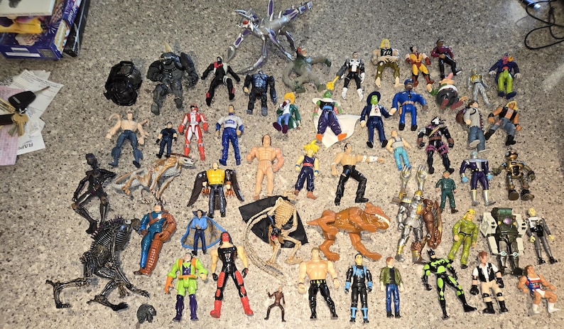May include: A collection of various action figures, including superheroes, monsters, and other characters. The figures are in various colors and poses, made of plastic, and are of different sizes.