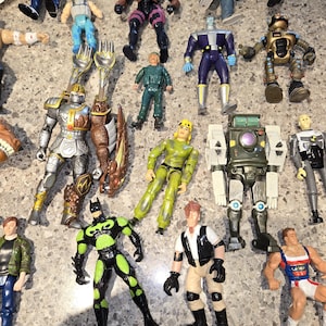 May include: A collection of various action figures, including superheroes, robots, and soldiers. The figures are in different colors and poses, with detailed designs. Some figures have weapons or accessories.