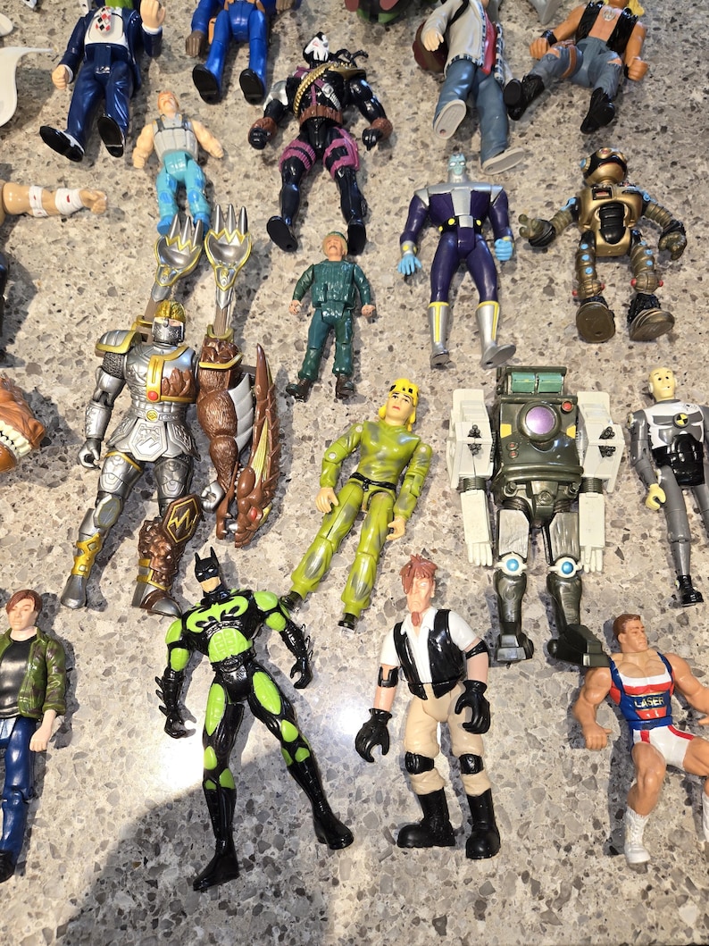 May include: A collection of various action figures, including superheroes, robots, and soldiers. The figures are in different colors and poses, with detailed designs. Some figures have weapons or accessories.