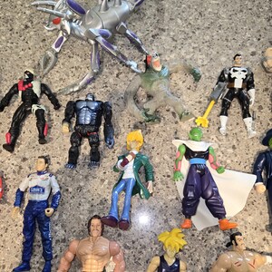 May include: A collection of action figures, including a silver and purple insect-like creature, a gorilla, and various superheroes. The figures are made of plastic and feature detailed designs and vibrant colors. The figures are on a gray surface.