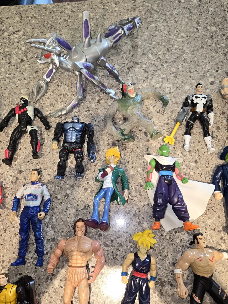 May include: A collection of action figures, including a silver and purple insect-like creature, a gorilla, and various superheroes. The figures are made of plastic and feature detailed designs and vibrant colors. The figures are on a gray surface.
