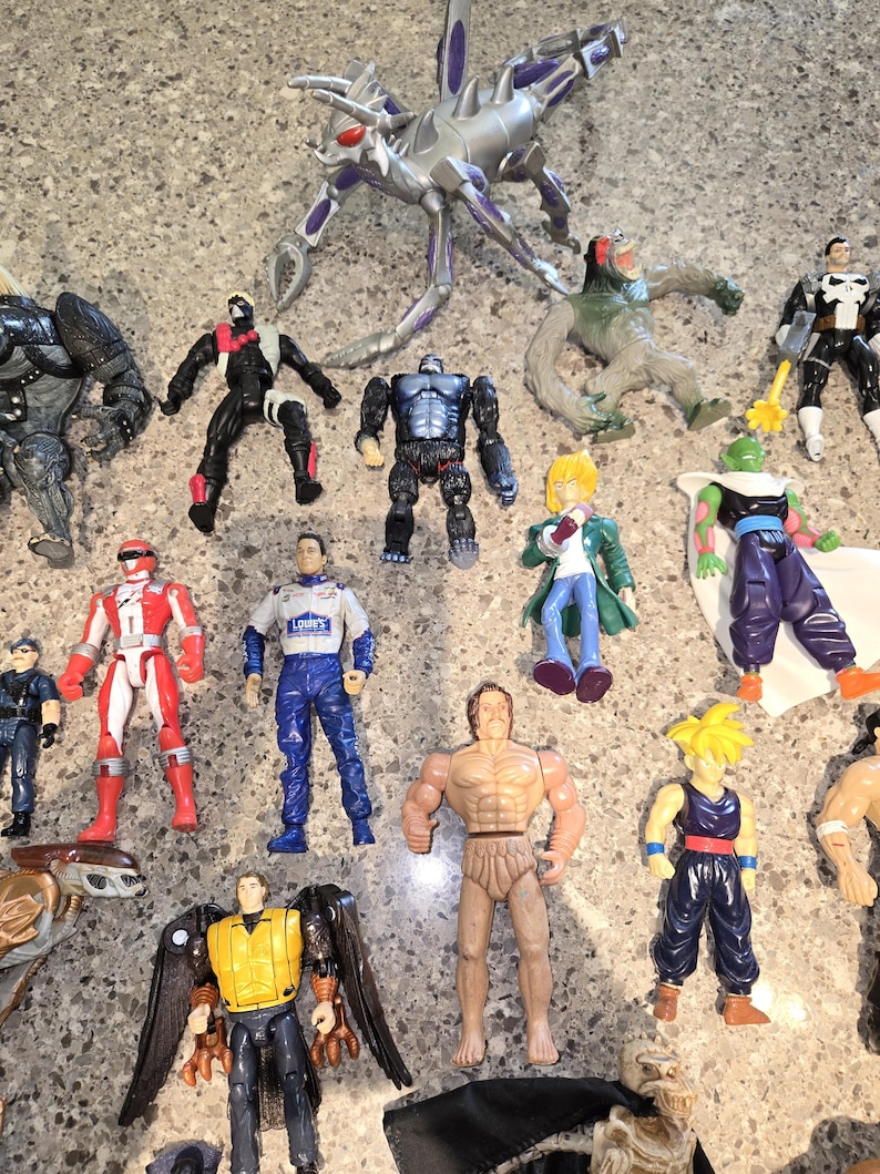 May include: A collection of various action figures, including a silver insect-like creature, a gorilla, a race car driver, and several superheroes. The figures are made of plastic and feature a range of colors and designs.