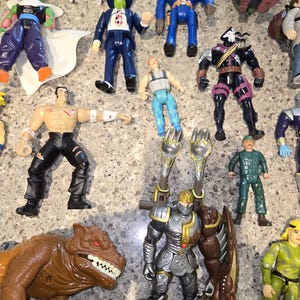May include: A collection of colorful action figures, including a blue police officer, a masked figure in a suit, a knight in silver armor, and a brown dinosaur-like creature. Various other characters are also visible.