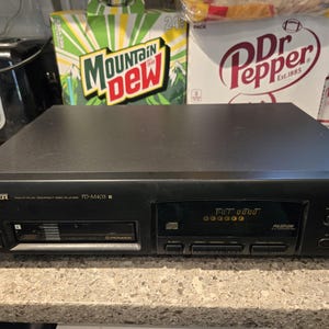 May include: A black Pioneer PD-M403 multi-play compact disc player featuring a front-loading disc tray, a digital display screen, and various control buttons. The unit has a rectangular chassis with branding and model text printed on the front panel.
