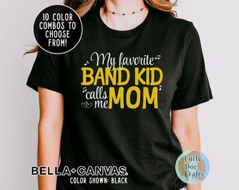 Może przedstawiać: Czarny T-shirt z napisem "My favorite band kid calls me Mom" w kolorze żółtym z nutami muzycznymi. Na dole koszulki znajduje się napis "BELLA+CANVAS".