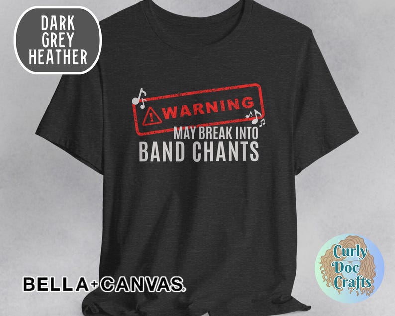 May include: Dark grey heather t-shirt with the text "WARNING MAY BREAK INTO BAND CHANTS" in white. The word "WARNING" is inside a red rectangle with musical notes. The shirt is from BELLA+CANVAS.