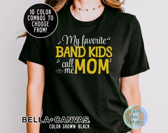 Może przedstawiać: Czarny T-shirt z napisem "My favorite band kids call me Mom" w białym i żółtym kolorze. Tekst jest otoczony nutami.