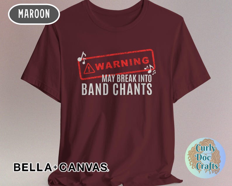 May include: Maroon t-shirt with the text "WARNING MAY BREAK INTO BAND CHANTS" in white. The word "WARNING" is inside a red rectangle with musical notes. The shirt is made of Bella+Canvas material.