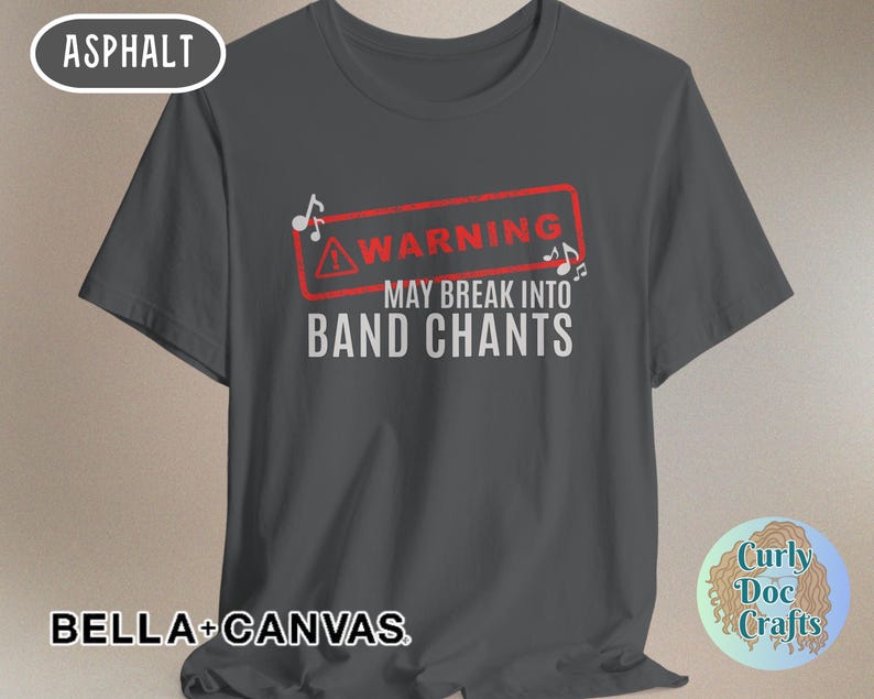 May include: Asphalt-colored t-shirt with the text "WARNING MAY BREAK INTO BAND CHANTS" in white. The warning is inside a red rectangle with musical notes. The shirt is from Bella+Canvas.
