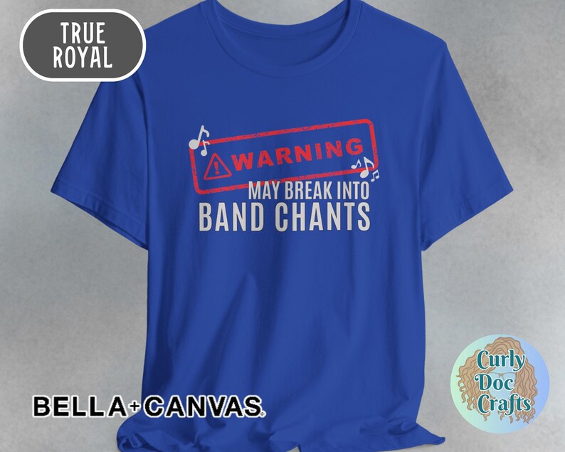 May include: Royal blue t-shirt with the text "WARNING MAY BREAK INTO BAND CHANTS" in white. The text is inside a red rectangle with musical notes. The shirt also has the text "BELLA + CANVAS".