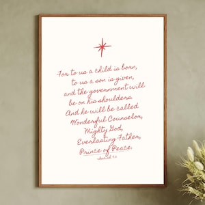 Puede incluir: Una impresión enmarcada con una estrella roja y escritura. El texto dice: "For to us a child is born...Prince of Peace. Isaiah 9:6." El marco es marrón y el fondo es blanco. La impresión se muestra en un mueble de madera.