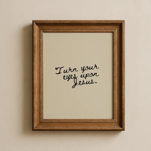 May include: A framed print with the text "Turn your eyes upon Jesus" in black script. The print has a cream-colored background and is encased in a brown wooden frame. The frame is rectangular and has a simple, classic design.