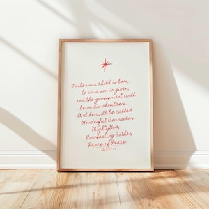 Puede incluir: Una impresión enmarcada con un marco de madera clara. La impresión presenta texto rojo con un gráfico de estrella en la parte superior. El texto dice: "For to us a child is born...Prince of Peace."