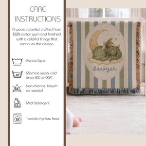 May include: A woven blanket featuring a green dragon sleeping on a cloud under a crescent moon with the name Sawyer printed below. The blanket has vertical blue and green stripes and a multicolored fringe edge, accompanied by care instructions.