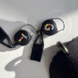 May include: Three black retractable keychains with a silver loop. The keychains have a small black cover on the end of the retractable cord. The keychains have colorful numbers on the front. The numbers are 1, 6, and 9.