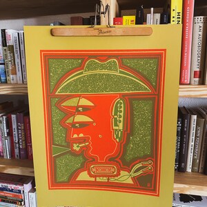 May include: A vintage-style poster featuring a stylized illustration of a person wearing a cowboy hat. The illustration is in shades of green, red, and yellow, with a textured background. The poster is printed on a yellow paper.