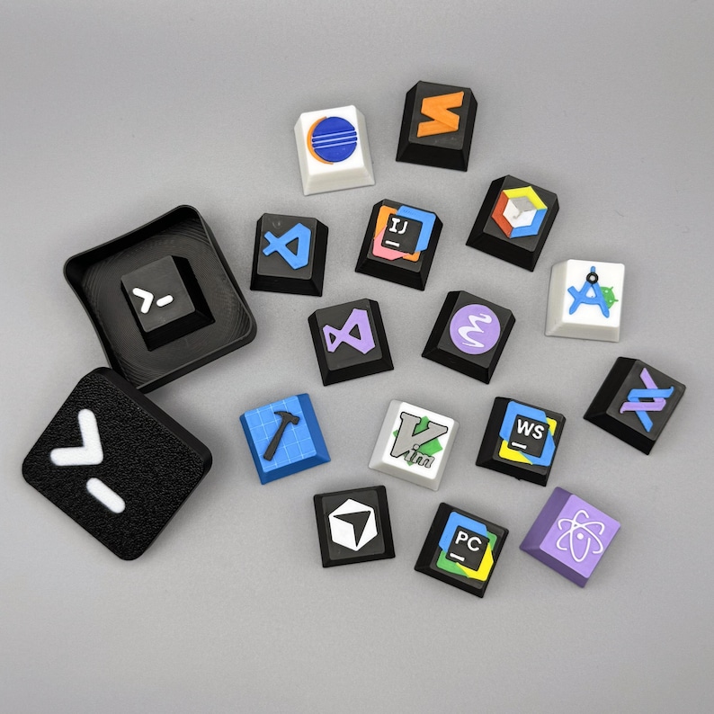 以下が含まれることがあります： さまざまなカラフルなデザインとシンボルが施されたカスタムキーキャップのコレクション。青とオレンジの円のデザインの白いキーキャップや、白い矢印のシンボルが付いた黒いキーキャップなど。メカニカルキーボード用のキーキャップです。