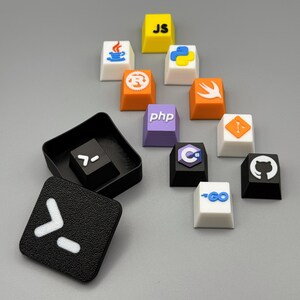 Puede incluir: Un conjunto de teclas personalizadas y coloridas, cada una con logotipos y s&iacute;mbolos de lenguajes de programaci&oacute;n. Incluye teclas con s&iacute;mbolos "JS", "PHP", "C" y "GO", adem&aacute;s de una tecla cuadrada negra con un s&iacute;mbolo blanco.
