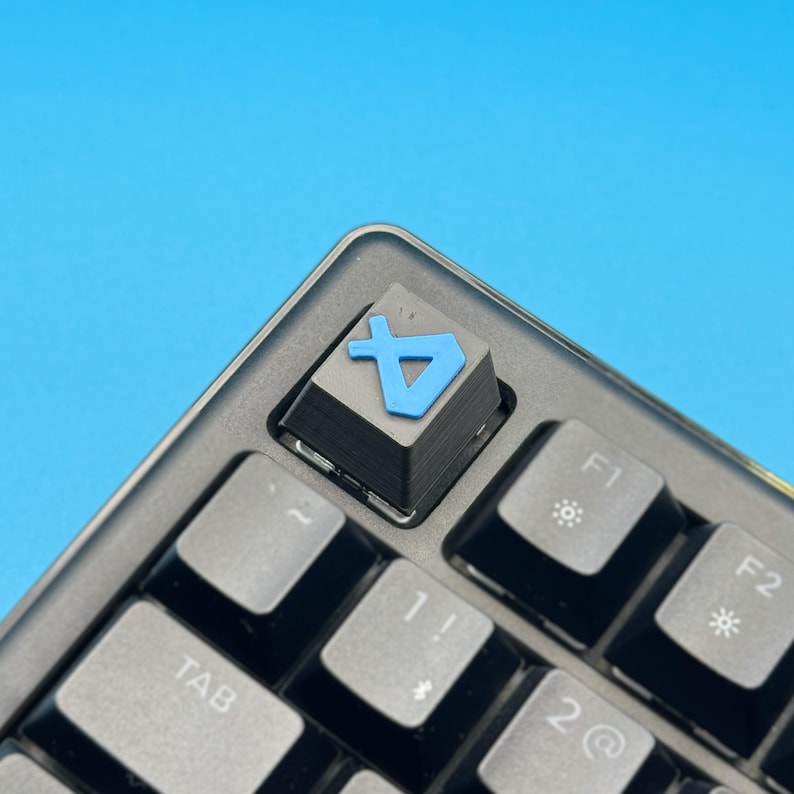 以下が含まれることがあります： 黒いメカニカルキーボードのクローズアップ。カスタムキーキャップが付いています。キーキャップは黒で、水色のシンボルが付いています。背景は単色の水色です。