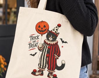 May include: A cream-colored canvas tote bag featuring a graphic of a black and white cat dressed as a clown in a red and black striped suit with a ruffled collar, holding an orange jack-o'-lantern balloon with the text TRICK OR TREAT.