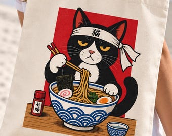 May include: A beige canvas tote bag featuring a graphic illustration of a black and white cat wearing a headband with the Japanese character for cat. The cat uses chopsticks to eat ramen from a bowl with a blue wave pattern and a red background.