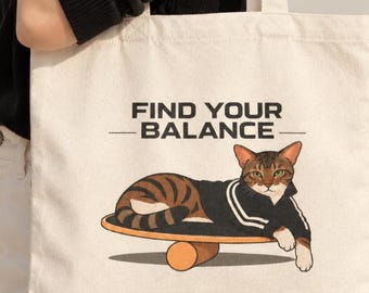 May include: A cream-colored canvas tote bag featuring a graphic illustration of a brown tabby cat wearing a black track jacket with white stripes, balancing on a wooden balance board, with the text FIND YOUR BALANCE printed above the cat.