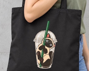 May include: A black tote bag featuring a graphic illustration of a Siamese cat inside a clear plastic cup with a lid and a green straw. The cat has dark brown ears, face, and paws, with a cream-colored body, and is holding onto the green straw.