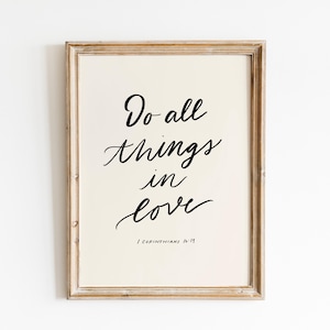 May include: A framed print with a white background and black calligraphy that reads "Do all things in love" with the scripture reference "1 Corinthians 16:19" below.