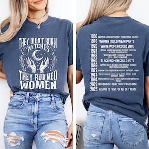 May include: A blue t-shirt with the text "They Didn't Burn Witches, They Burned Women" in white. The back of the shirt lists historical milestones for women's rights, including the right to vote and equal pay.