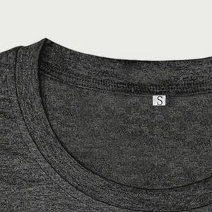May include: Close-up of a dark gray t-shirt neckline. The shirt has a crew neck and a small white tag with the letter "S" on it. The fabric has a textured appearance.