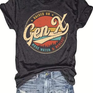Puede incluir: Camiseta gris oscuro con un dise&ntilde;o gr&aacute;fico circular retro que dice "Raised on Gen X Hose Water & Neglect". La camiseta se combina con pantalones cortos de mezclilla.